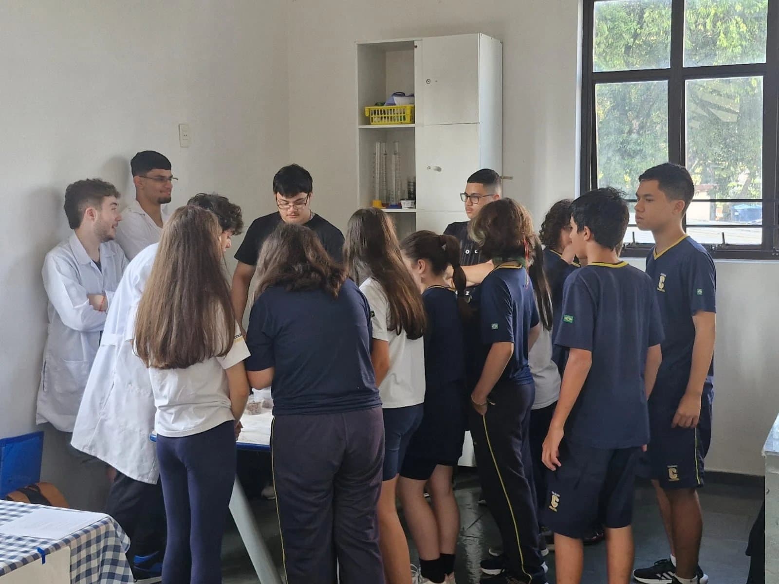 Alunos do Ensino Médio, de jaleco, explicam um experimento para alunos do Fundamental no laboratório