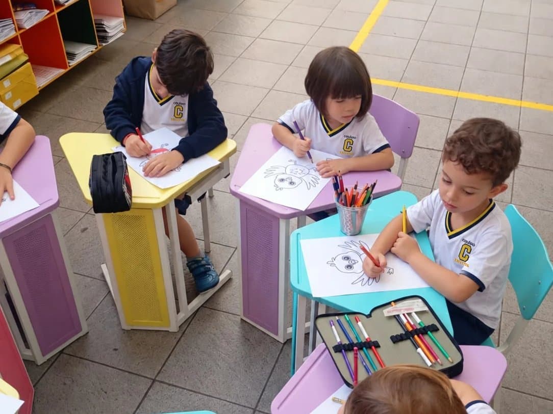 Crianças da Educação Infantil pintam desenhos com lápis de cor nas carteiras coloridas