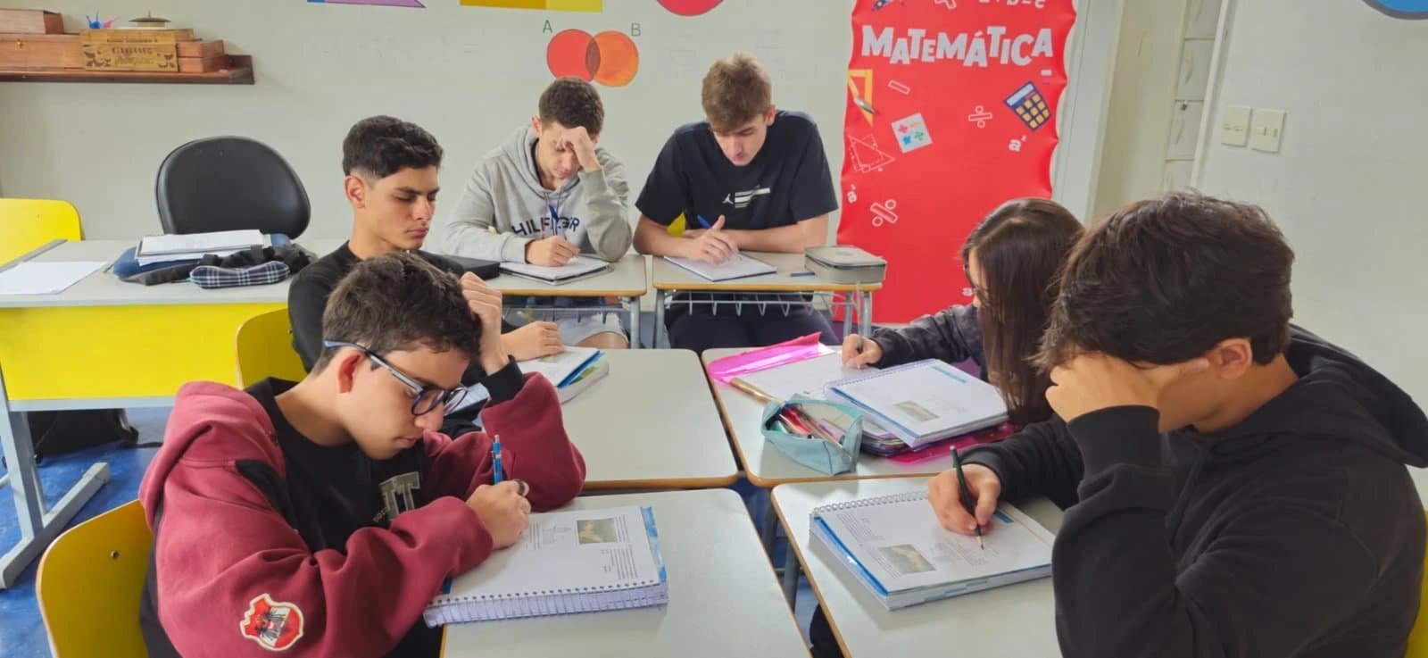 Alunos do Ensino Médio estudam nas carteiras, com o painel de Matemática ao fundo