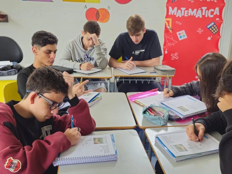 Alunos do Ensino Médio estudam nas carteiras, com o painel de Matemática ao fundo