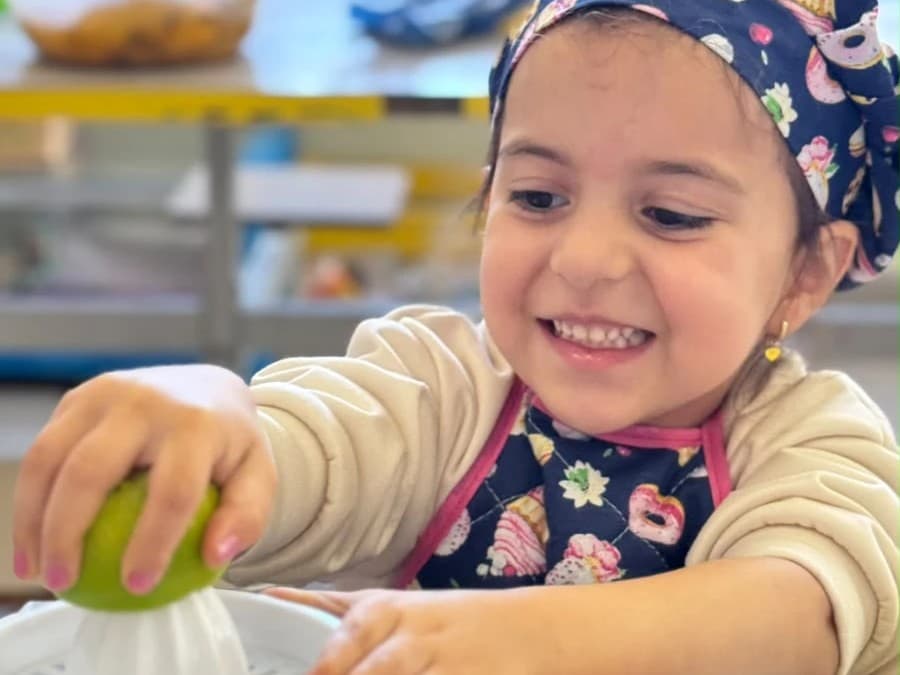 Menina de touca e avental espreme um limão ao preparar o próprio lanche
