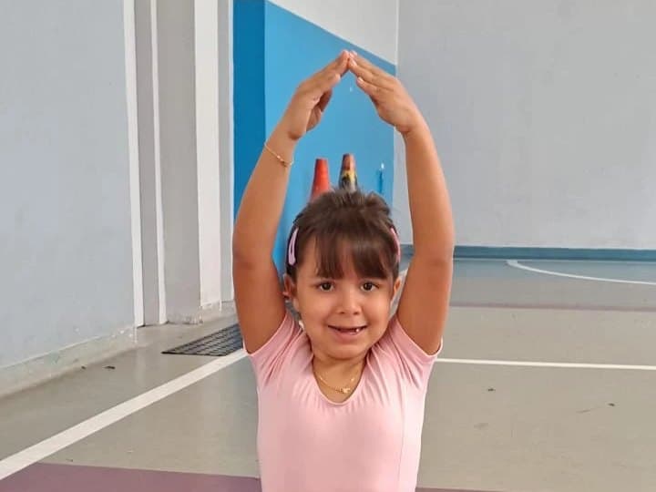 Aluna de ballet com os braços erguidos acima da cabeça, na quadra da escola