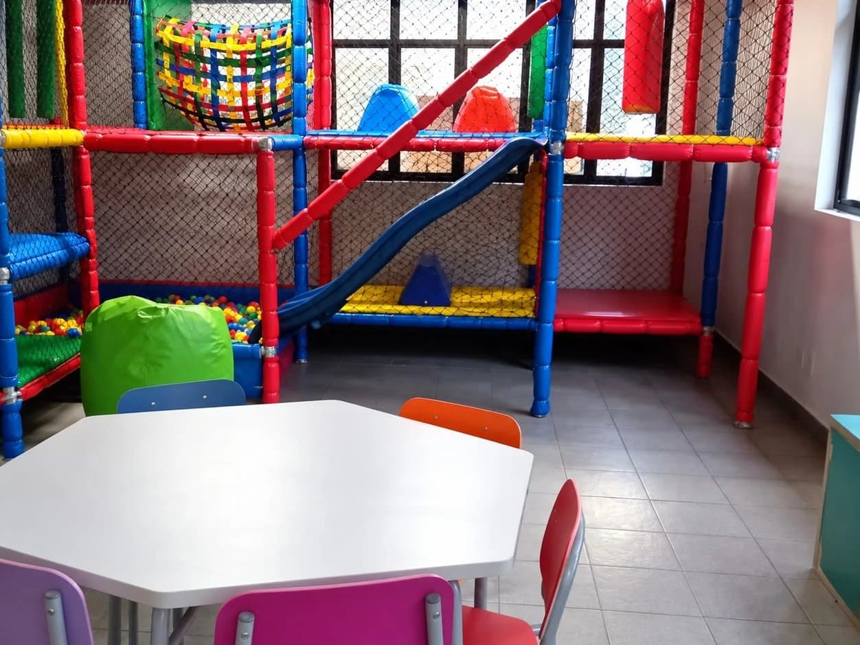 Espaço Multifuncional com brinquedão colorido, piscina de bolinhas e mesa com cadeiras coloridas