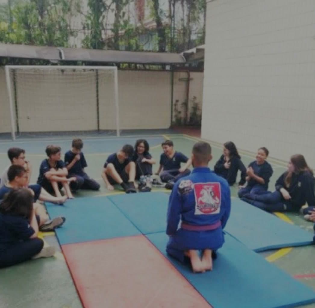 Turma sentada no tatame durante a aula de judô na quadra