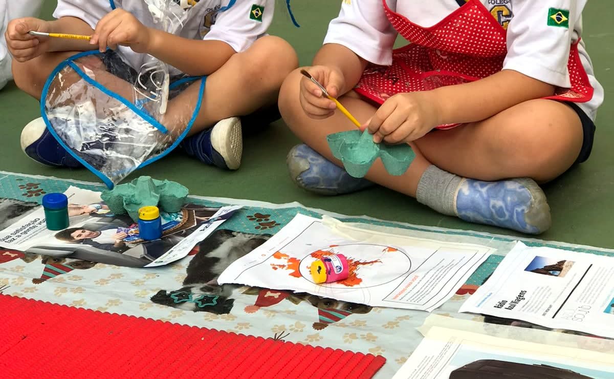 Mãos de crianças recortando e colando papéis coloridos numa atividade de artes